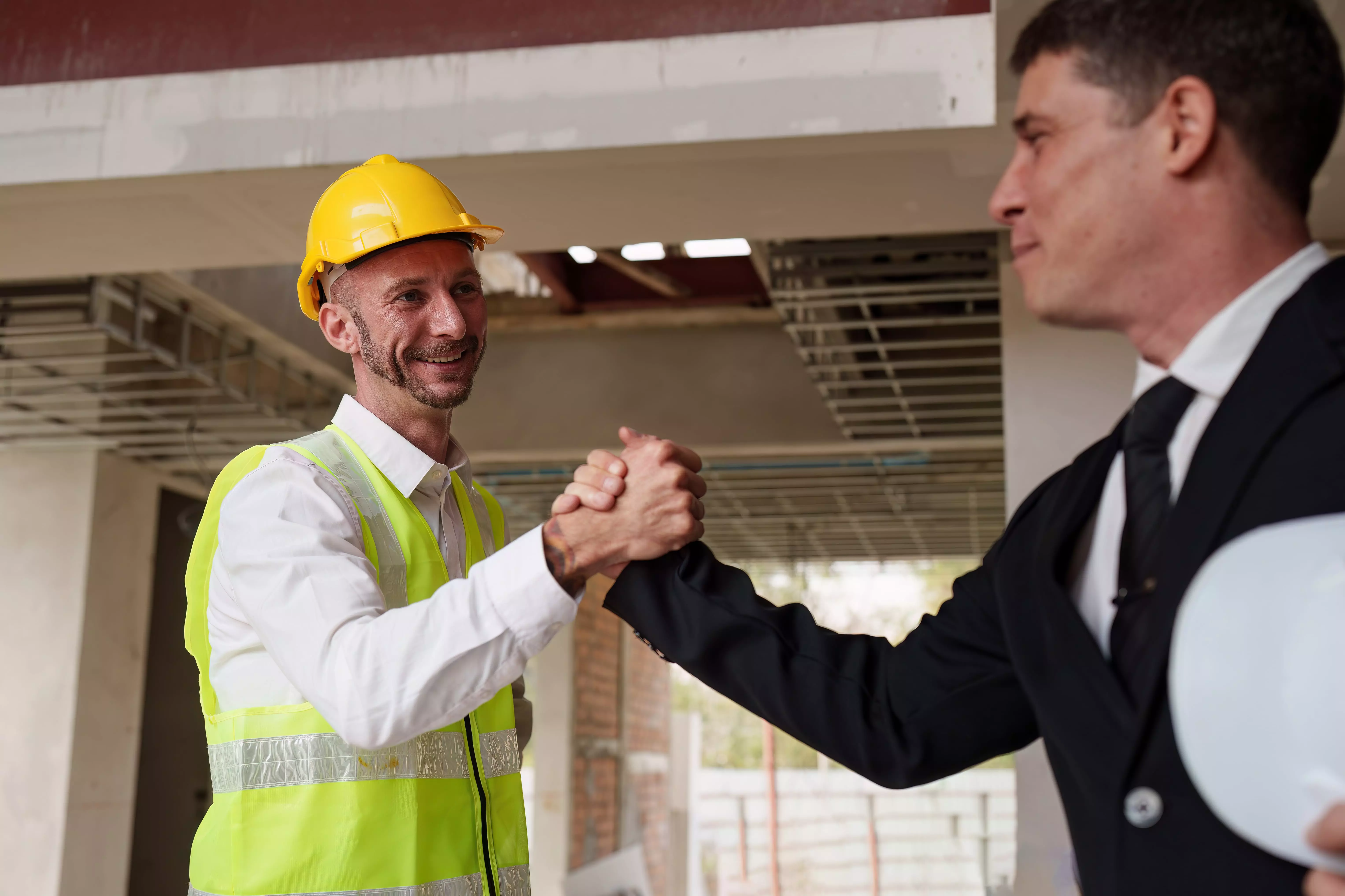 alt="A professional in a suit shaking hands with a worker in a construction helmet, representing partnership and collaboration."