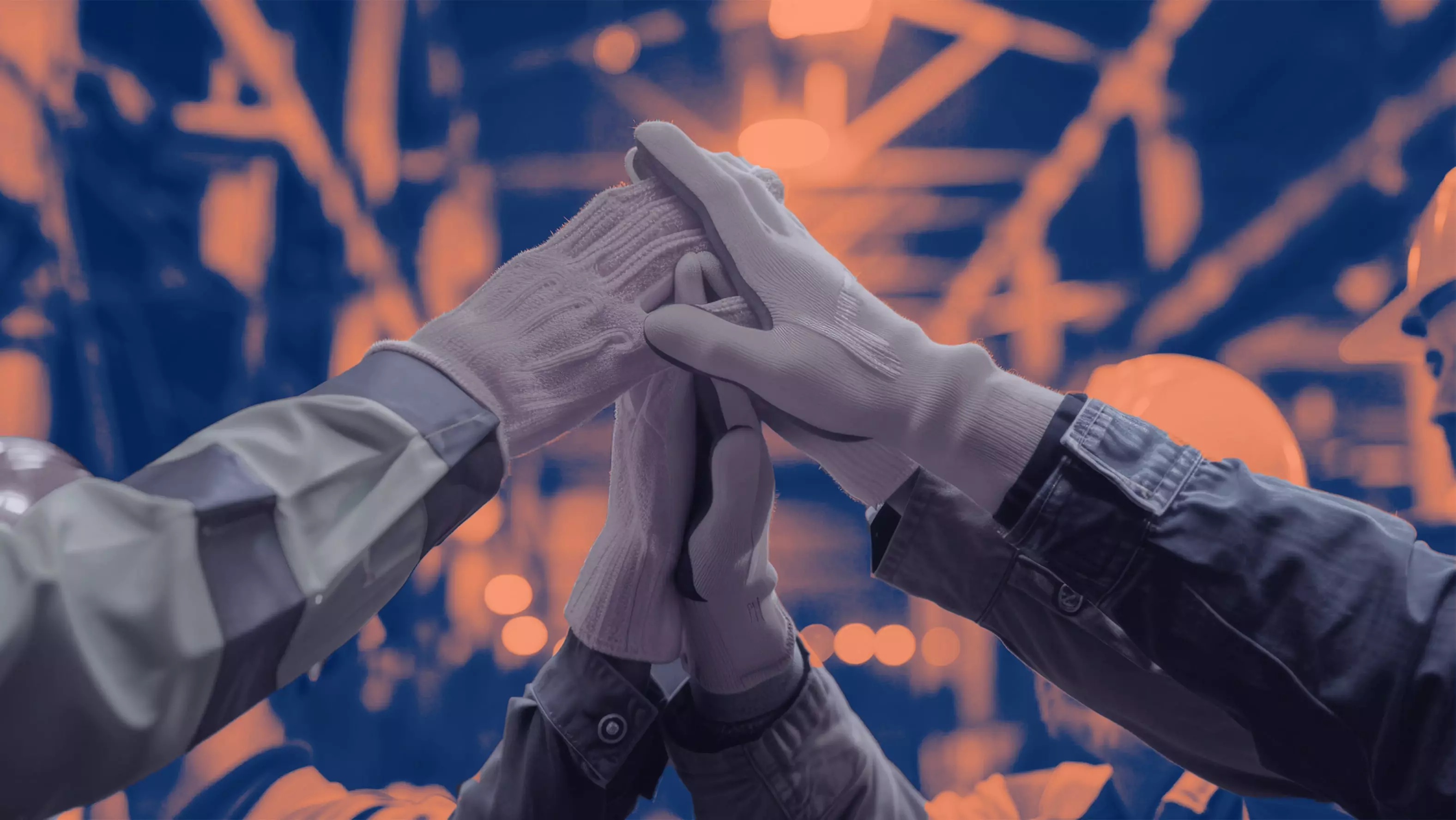 United for Success: Teamwork at the Core Close-up of construction workers wearing gloves, joining hands together in a teamwork gesture against a blurred industrial background.