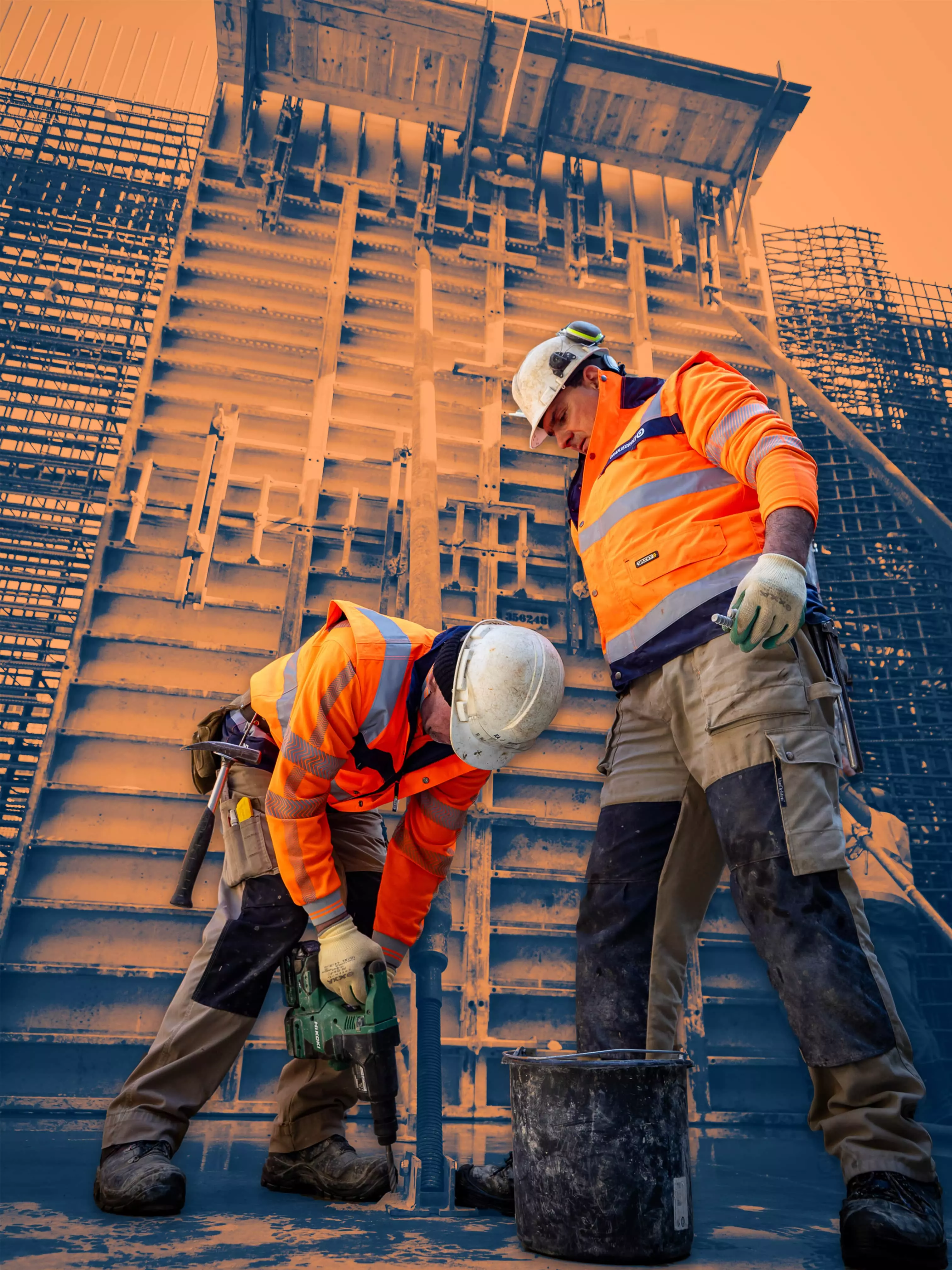 Building Strong Foundations, One Wall at a Time Two construction workers in orange safety vests working near a large vertical formwork structure on a building site.