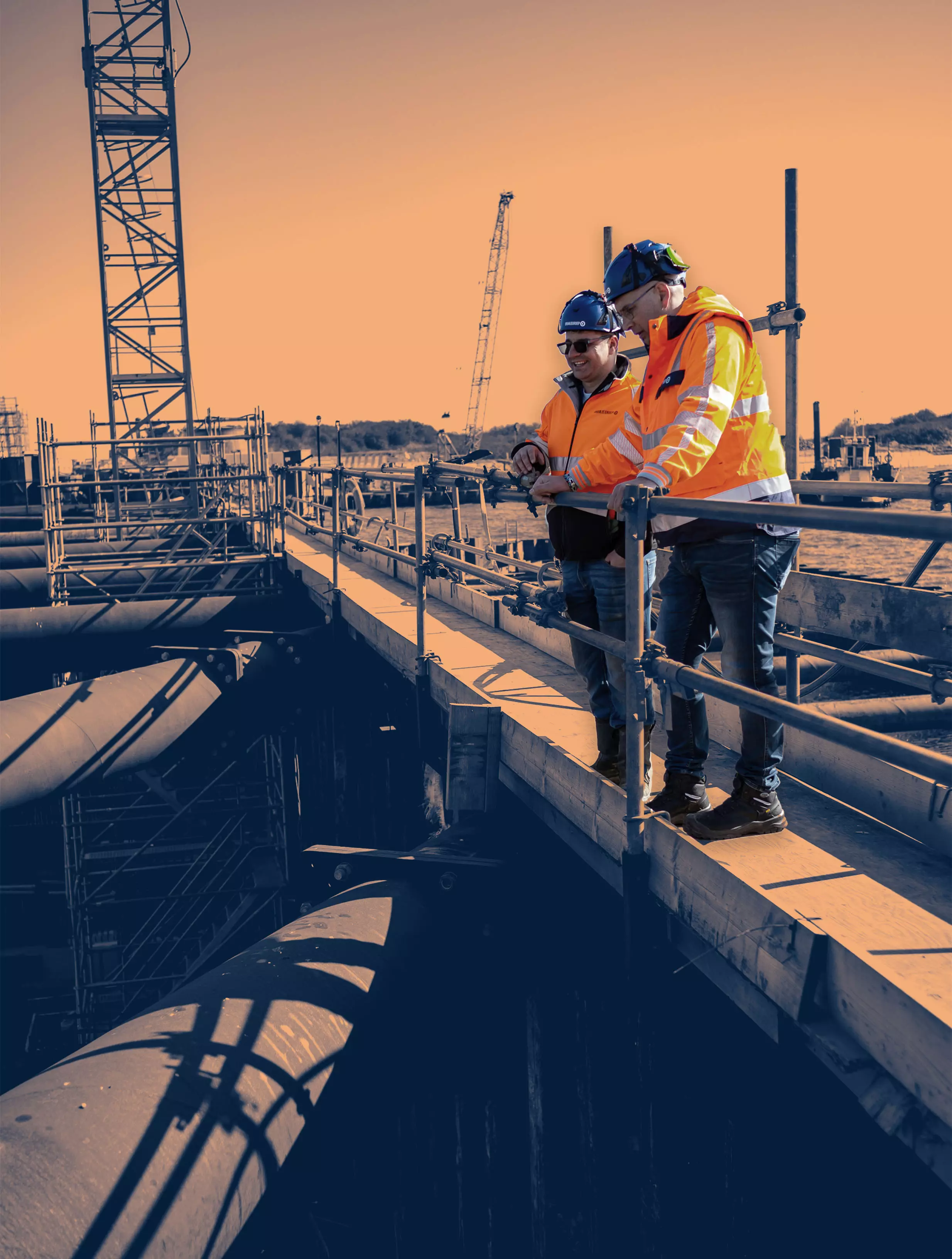 Shared Success Begins on Site Two construction supervisors in safety gear discussing project progress on-site, standing on a platform above large industrial pipes.